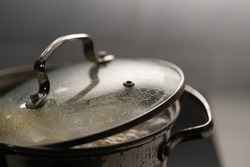 A saucepan on the stove in the kitchen. Boiling bubbling water while cooking. Boiled potatoes, vegetables or soup. The dishes are covered with a lid.