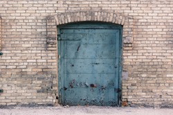 Old blue rusted door in industrial area against light colored brick wall