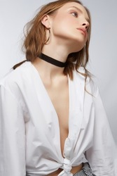 Cropped shot of a slim blonde lady with a gentle makeup on a light background. The attractive tempting girl is wearing a white blouse, striped pants gold earrings and a black soft velvet choker.