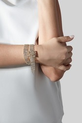 Cropped close-up shot of a woman with a gold rhinestone bracelet with a buckle. The woman in a white blouse is wearing a rhinestone bracelet on a light background. Front view.