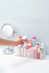       Close-up shoot of a transparent universal organizer with 5 compartments of different shapes and sizes. The woman is taking cosmetic products out of the organizer on a white table. Top view.     