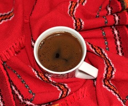 Photo of frothy Turkish coffee in a large cup on a red ethnic and vintage patterned cover