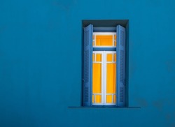 Window at night from outside. Illuminated window with open shutters against blue wall.