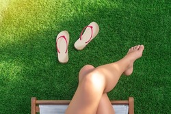 Selective focus of a girl sitting in a hammock on artificial turf with bare feet and flip-flops on the grass