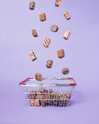 Chocolates falling in basket on purple background. Minimal concept of buying sweets. Creative chocolate obsession idea. Going away from diet to buy box of chocolates.