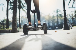 Back view of young hipster girl balancing on electric hoverboard at the sunny park, active woman using and driving on segway outdoor, film effects, flare light