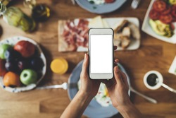 Closeup of female hands holding modern smartphone with blank screen for your text message or design, order food online concept, mock-up of mobile phone, tasty breakfast on the background