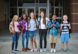 Large Group portrait of pre-adolescent school kids smiling in front of the school building. Back to school photo of a diverse group of children wearing backpacks and ready to go to school