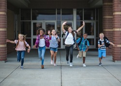 Group of school kids running as they leave the school building Back to school photo of a diverse group of children wearing backpacks and ready to go home from school