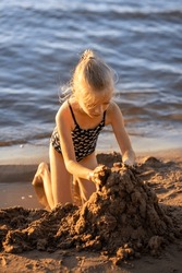 A little girl makes a sand castle on the river bank. A child plays in the sand on the beach. Summer children's games on the sea.