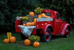 A vintage red classic old truck filled season flowers hay and festive fall orange pumpkins. 