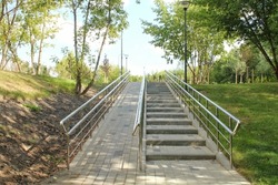 Stairs and ramp with metal railings for the passage of strollers and wheelchairs in public park. Concept of comfortable barrier-free urban environment in city. Pathway for people with disabilities