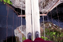 Hiker looking down at feet at river below on a rope bridge in Norway