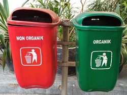 Different colored trash cans with non organic and organic waste suitable for recycling, outside against plant. Segregate waste, sorting garbage, waste management.  
