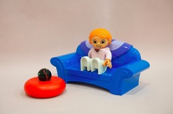 Lego girl sits on a blue sofa, next to a red stand with a black ball