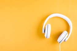 Minimalistic top view composition with white headphones on bright yellow background with a lot of copy space for your text. Close up,  flat lay.