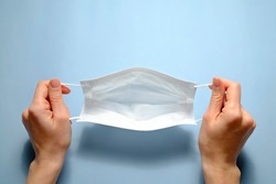 First person view of a woman holding face mask over blue textured table background. Protective raspiratory mask for spreading virus. Close up, copy space, top view, flat lay.