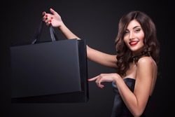 Sale. Young smiling woman showing shopping bag in black friday holiday. Girl on dark background with copy space