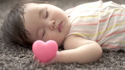 closeup of sleeping baby holding heart symbol in the living room