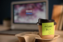 Back to Work Concept. Closeup of Welcome Note on Takeaway Coffee Cup in Office Desk. Message from a Colleague or Boss  