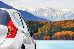 Road Trip Concept, Car Driving Travel in Fall and Autumn Season, Lake, beautiful Foliage and Mountains covered by Snow as background