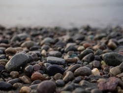 Pebbles on the seashore close-up. Rocky beach. Stones close-up with bokeh. Gray natural background. Autumn on the seashore. Waves and wet pebbles