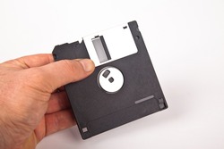 Old computer and data storage technology, hand held black plastic magnetic floppy disk 3½ inches, isolated on white background