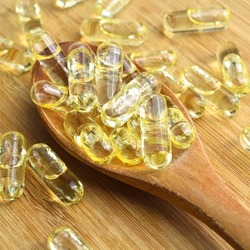Yellow fish oil oval tablet pills in wooden spoon on bamboo cutting board, medical oval pills tablets