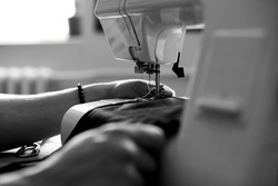 Black and white photo of Man sews clothes on sewing machine,  male tailor working with sewing in atelier, textile industry, hobby, workspace, small busines. Creation process DIY