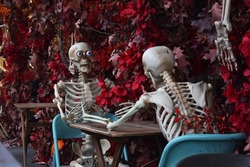 Halloween street decor. In the restaurant, skeletons sit at the table and communicate with each other. Fallen red leaves. Autumn festival.