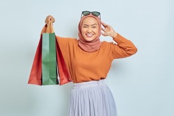 Portrait of cheerful Asian Muslim woman in brown sweater and hijab holding shopping bag with purchases after shopping isolated on white background. World Consumer Rights Day Concept