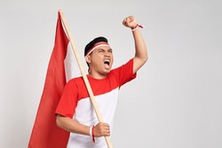 Excited young Asian man standing holding Indonesian flag with raised hands while Celebrate Indonesia independence day on 17 August isolated over white background