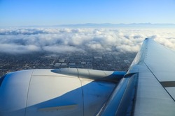 Sitting on the airplane, through the window overlooking the ground. Background is sea ​​of ​​clouds, buildings and blue sky.