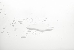 Water puddles and droplets on white reflective surface. Frontal view and deep focus.
