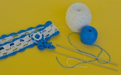 A hair band made of white and blue cotton threads crocheted, threads and a crochet hook on a yellow background, diy.