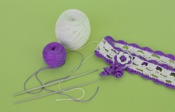 A hair band made of white and purple cotton threads crocheted, threads and a crochet hook on a green background, diy.