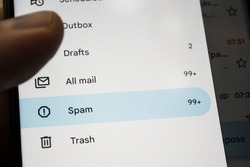A human finger in the gloom, pressing a spam button in a mail program, on a blurred background of a smartphone screen. Fight spam and advertising marketing campaigns.