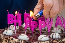 They light a fire on birthday candles on a cake from a lighter, a festive table in an apartment, a selective focus.