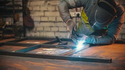 A man worker welding the seams between the metal beams indoors