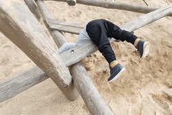 A little boy playing on a children's playground - flips himself over wooden log