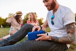 young hipster company of friends having fun together in park smiling listening to music on wireless speaker, summer style season