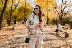 attractive young woman walking in autumn park with coffee wearing checkered coat, sunglasses, happy mood, fashion style trend