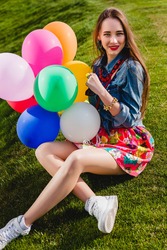 young stylish hipster teen girl happy smiling, park, air balloons birthday party, cool accessories, red lipstick makeup, colorful, sunny, have fun, sitting on grass, denim shirt, braces, laughing