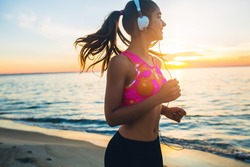 young beautiful woman jogging on beach, morning, fitness outfit, listening to music on headphones, smartphone, sea sunrise, skinny perfect slim body, healthy living lifestyle, summer, smiling, happy