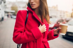 stylish beautiful woman walking in street in red coat, autumn fashion trend, holding coffee in paper cup in hand