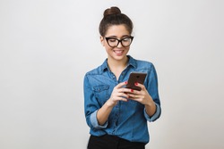 pretty young woman holding smart phone, using device, wearing stylish glasses, smiling, isolated on white background, denim shirt