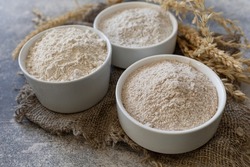 Food and baking ingredient. Wheat flour coarse from whole wheat grains, wheat bran and wheat flour over gray stone background.