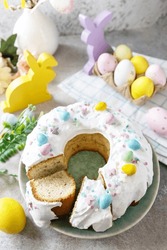Glazed easter lemon cake decorated with confectionery and mini chocolate eggs candy on gray stone background. Happy Easter holidays, tasty dessert. 