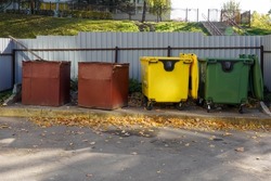 Photo of yellow, red and green trash cans with rubbish on the street in the city.