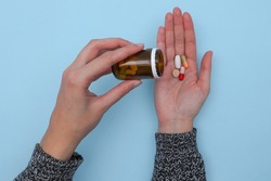 Elderly sick ill woman hold four different pills in her hand palm after spilling from bottle. Take painkiller supplement medicine, old senior people pharmaceutical healthcare treatment concept.